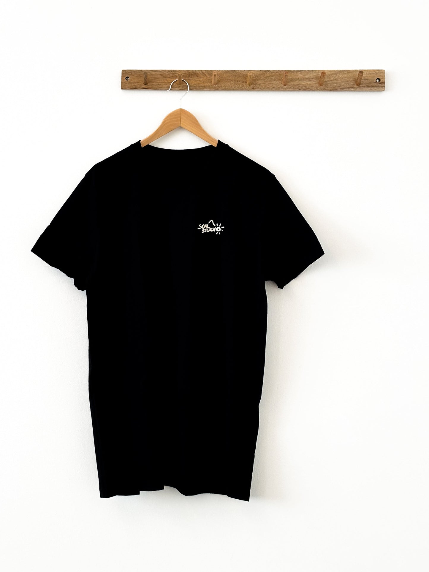 Black t-shirt with a white SOAL Studio logo on a wooden hanger against a white background
