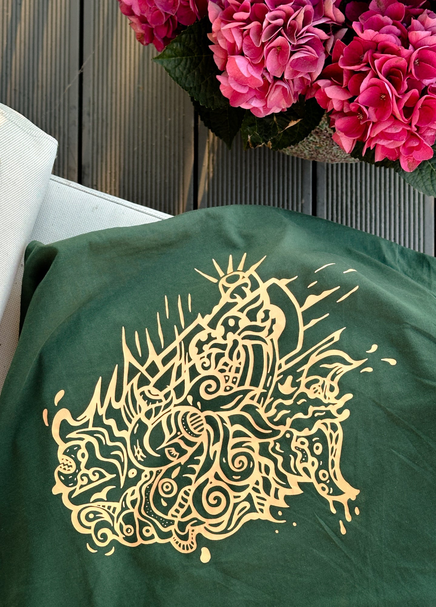 SOAL Studio - batch#1 Green garment with orange dragon design next to pink flowers on a wooden surface