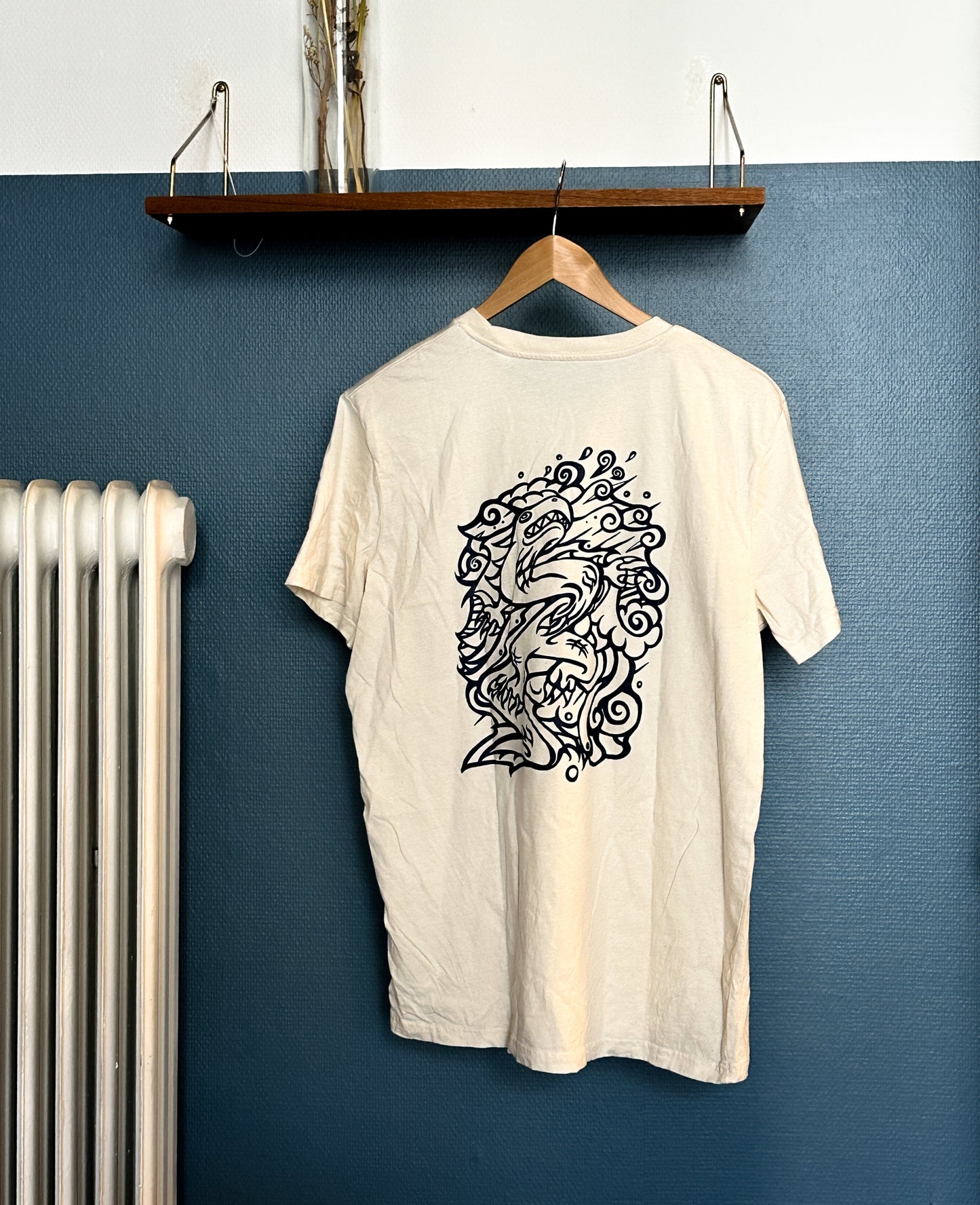 Beige SOAL Studio t-shirt with Navy graphic art Dragon hanging on a wooden hanger against a blue wall.