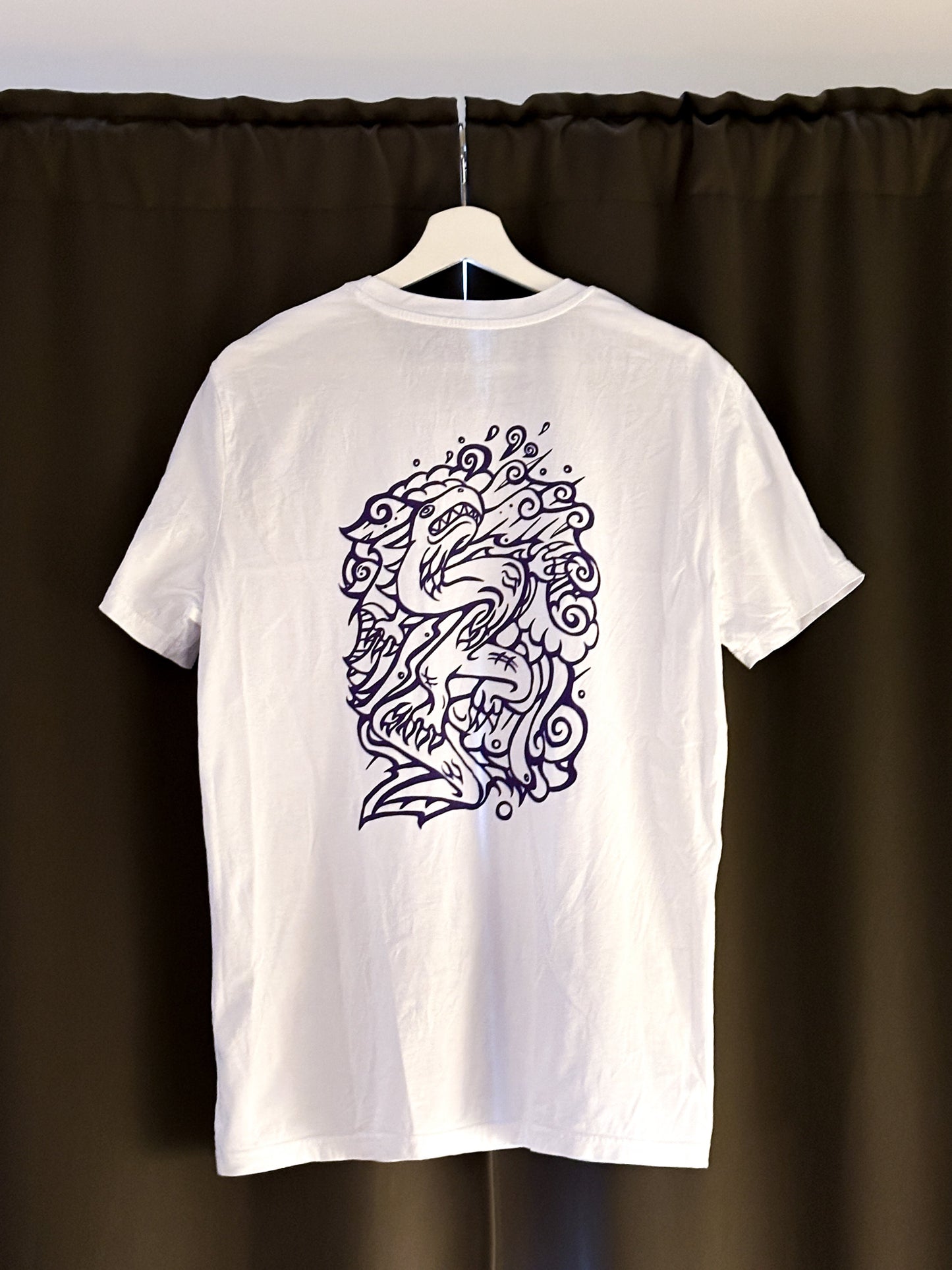 White SOAL Studio t-shirt with a purple dragon design on a hanger against a dark curtain background