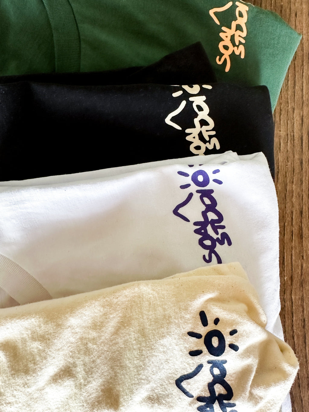 All Editions of SOAL Studio art-shirts Batch #1 - Folded t-shirts with brand logos on a wooden surface